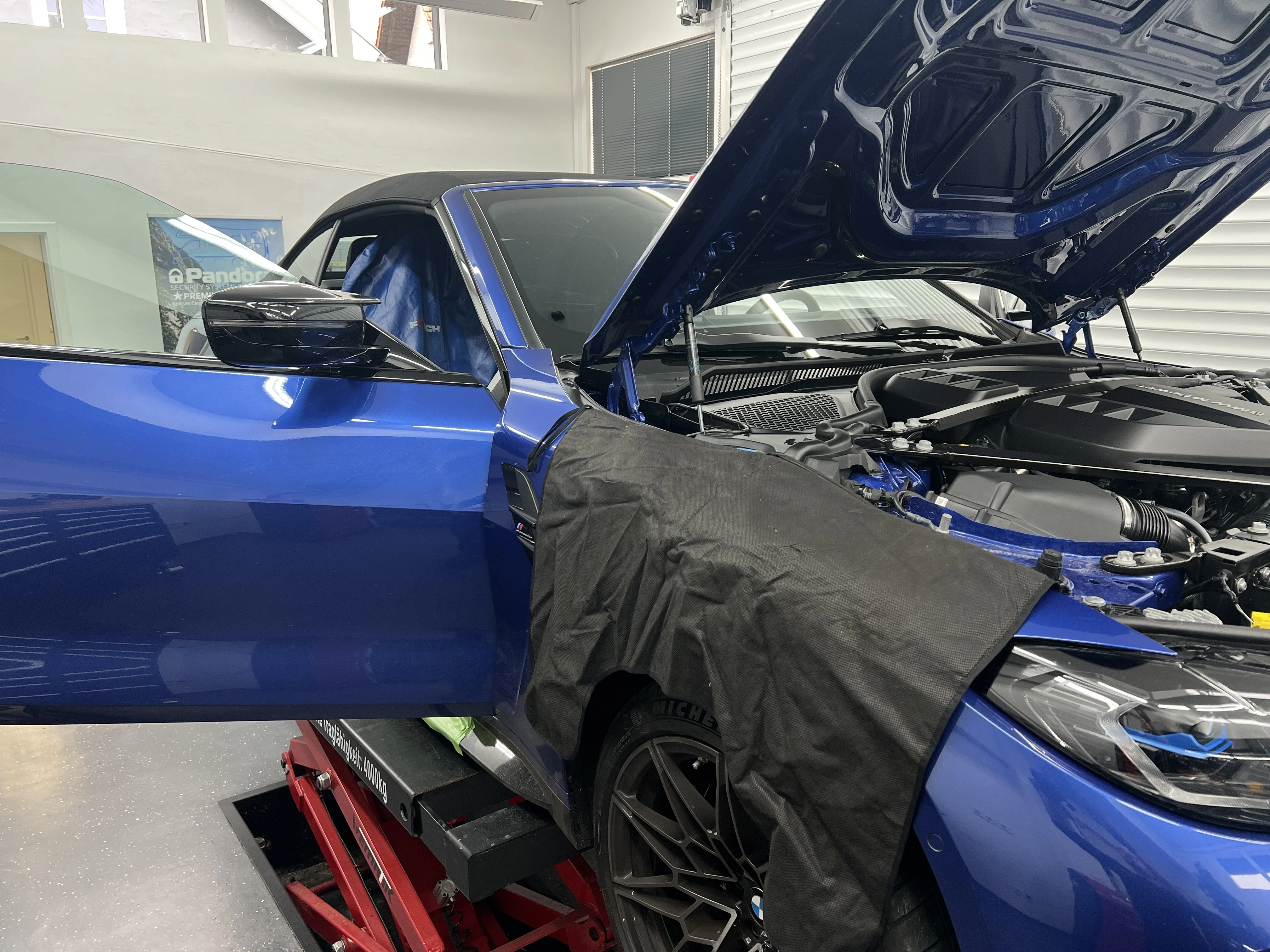 BMW Cabrio mit Schutzmatte über dem Kotflügel und blauem Sitzschutz bei geöffneter Motorhaube