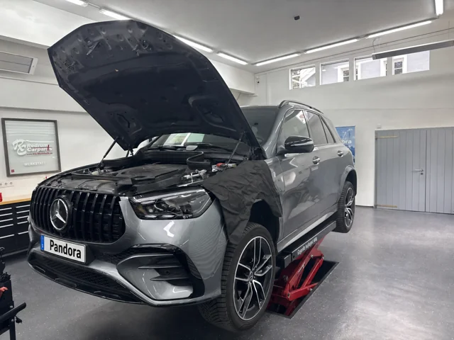 Mercedes-Benz GLC mit geöffneter Motorhaube und Schutzauflage in der Werkstatt.